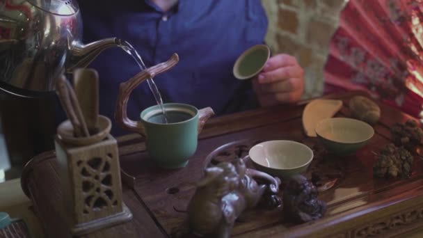 Un hombre vierte agua hirviendo de una tetera en una tetera para preparar té en una sala de té — Vídeo de stock