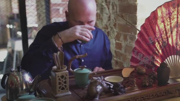 Een man drinkt groene thee uit een theeservies in een theekamer — Stockvideo