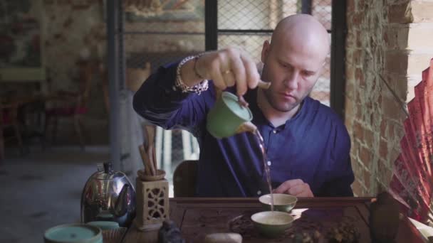 Un bărbat toarnă ceai în cești de ceai pe o tavă de lemn într-o cameră de ceai — Videoclip de stoc