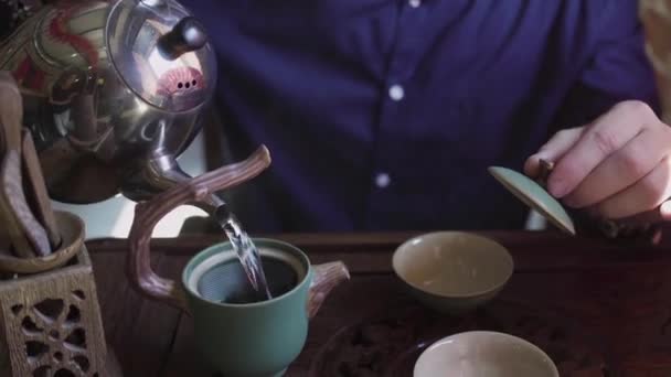 Un hombre vierte agua hirviendo de una tetera en una tetera para preparar té en una sala de té — Vídeos de Stock