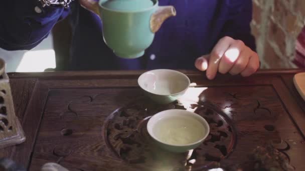 Ένας άνθρωπος ρίχνει τσάι σε φλιτζάνια τσαγιού σε ένα ξύλινο δίσκο σε μια αίθουσα τσαγιού — Αρχείο Βίντεο