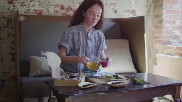 La chica está sentada en la mesa y vierte té verde en una taza de té y lo prueba — Vídeo de stock