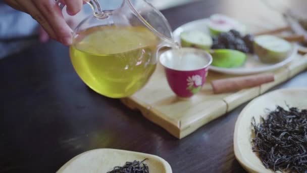 Uma mão das mulheres derrama chá verde em uma xícara de chá na mesa — Vídeo de Stock