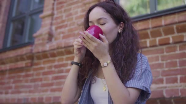 Una hermosa chica de pelo rizado bebe té y disfruta de su sabor en la calle — Vídeo de stock