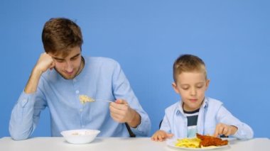 Bir adam ve bir çocuk masada oturuyorlar, adam yulaf lapası yiyor, ve çocuk fast food yiyor. Sağlıklı ve sağlıksız gıda kavramı. Fast food