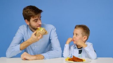 Genç bir adam ve bir çocuk masada oturuyorlar, adam çocuğun fast food yemesine izin vermiyor. Sağlıklı ve sağlıksız gıda kavramı. Fast food