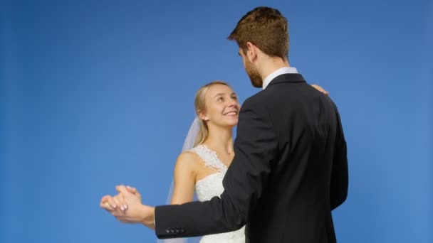Braut und Bräutigam in Hochzeitsanzügen tanzen auf blauem Grund. Hochzeit — Stockvideo