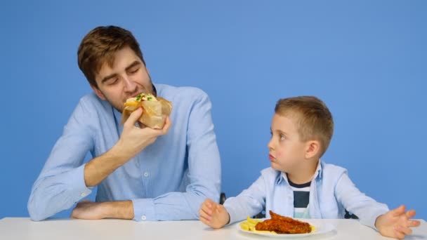 Молодой человек и мальчик сидят за столом, мужчина не позволяет мальчику есть фаст-фуд. Понятие здоровой и нездоровой пищи. Фаст-фуд — стоковое видео