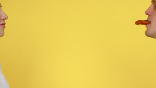 Close-up de uma mulher e um homem que estão comendo pepitas e beijando ternamente em um fundo amarelo. O conceito de comida saudável e insalubre. Fast food — Vídeo de Stock