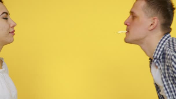 Primer plano de una mujer y un hombre que están comiendo papas fritas y besándose tiernamente sobre un fondo amarillo. El concepto de comida saludable y poco saludable. Comida rápida — Vídeo de stock