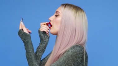 Bir kız dudaklarını kırmızı rujla boyuyor ve mavi arka planda zevkle hamburger yemeye başlıyor. Diyet olsun. Sağlıklı ve sağlıksız gıda kavramı. fast food