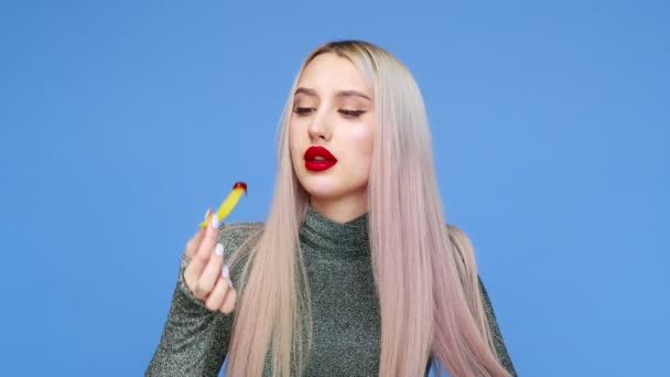 Close-up de uma menina pinta os lábios com batom vermelho e começa a comer um hambúrguer com prazer em um fundo azul. Dieta. O conceito de comida saudável e insalubre. fast food — Vídeo de Stock