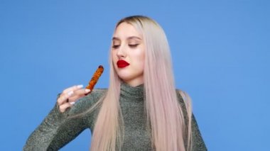 Dudaklarını kırmızı rujla boyayan bir kızın yakın plan fotoğrafı. Makyajını bozmamak için dikkatlice yiyor. Mavi arka planda. Diyet olsun. Sağlıklı ve sağlıksız gıda kavramı. fast food