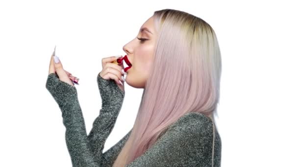 Close-up van een meisje schildert haar lippen met rode lippenstift en begint met plezier een hamburger te eten op een witte achtergrond. Dieet. Het concept van gezond en ongezond voedsel. fast food — Stockvideo