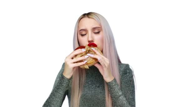 Közelkép egy lányról, piros rúzzsal az ajkain, hamburgert eszik és rúzst keneget a kezével fehér háttéren. Fogyókúra. Az egészséges és egészségtelen ételek fogalma. gyorsétterem — Stock videók