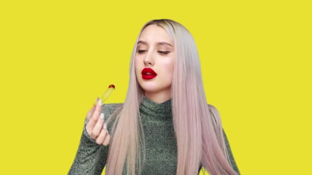 Close-up van een meisje schildert haar lippen met rode lippenstift en begint met plezier een hamburger te eten op een gele achtergrond. Dieet. Het concept van gezond en ongezond voedsel. fast food — Stockvideo