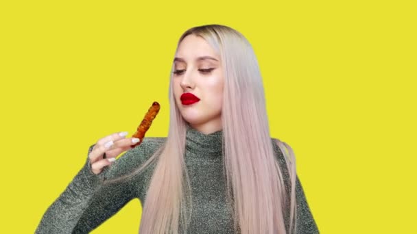 Крупный план девушки, которая покрасила губы красной помадой, ест осторожно, чтобы не испачкать макияж. На жёлтом фоне. Диета. Понятие здоровой и нездоровой пищи. фастфуд — стоковое видео