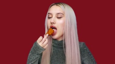 Kırmızı arka planda cinsel açıdan fast food yiyen güzel bir kızın yakın çekimi. Diyet olsun. Sağlıklı ve sağlıksız gıda kavramı. fast food