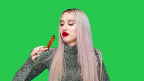 Κοντινό πλάνο μιας κοπέλας που έβαψε τα χείλη της με κόκκινο κραγιόν, τρώει προσεκτικά για να μην μουτζουρώσει το μακιγιάζ της. Σε πράσινο φόντο. Δίαιτα. Η έννοια των υγιεινών και ανθυγιεινών τροφίμων. fast food — Αρχείο Βίντεο