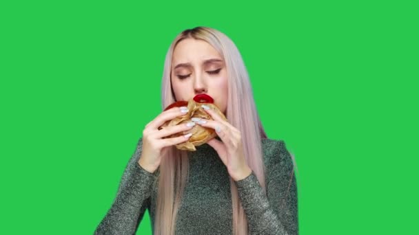 Närbild av en flicka med rött läppstift på läpparna, äta en hamburgare och smeta läppstift med handen på en grön bakgrund. Föda. Begreppet hälsosam och ohälsosam mat. snabbmat — Stockvideo