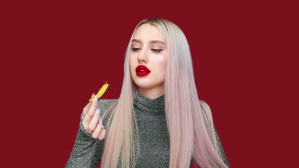 El primer plano de una chica se pinta los labios con lápiz labial rojo y comienza a comer una hamburguesa con placer sobre un fondo rojo. Dieta. El concepto de comida saludable y poco saludable. comida rápida — Vídeo de stock