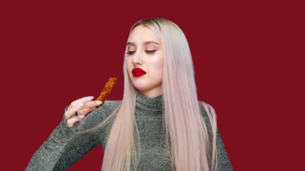 Närbild av en flicka som har målat sina läppar med rött läppstift, äter noggrant för att inte smeta hennes makeup. På en röd bakgrund. Föda. Begreppet hälsosam och ohälsosam mat. snabbmat — Stockvideo