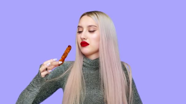 Närbild av en flicka som har målat sina läppar med rött läppstift, äter noggrant för att inte smeta hennes makeup. På en lila bakgrund. Föda. Begreppet hälsosam och ohälsosam mat. snabbmat — Stockvideo