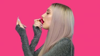 Dudaklarında kırmızı ruj lekesi olan, hamburger yiyen ve elini pembe arka plana sürerek ruj süren bir kızın yakın çekimi. Diyet olsun. Sağlıklı ve sağlıksız gıda kavramı. fast food