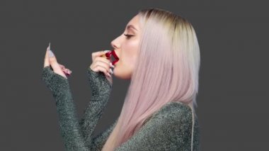 Bir kız dudaklarını kırmızı rujla boyuyor ve gri arka planda zevkle hamburger yemeye başlıyor. Diyet olsun. Sağlıklı ve sağlıksız gıda kavramı. fast food