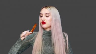 Dudaklarını kırmızı rujla boyayan, makyajını kirletmemek için dikkatlice yiyen bir kızın yakın çekimi. Gri bir arka planda. Diyet olsun. Sağlıklı ve sağlıksız gıda kavramı. fast food