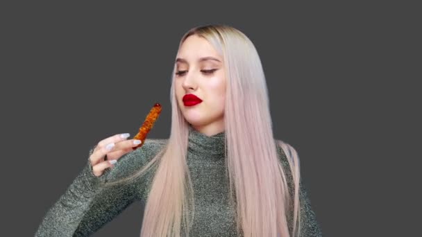 Närbild av en flicka som har målat sina läppar med rött läppstift, äter noggrant för att inte smeta hennes makeup. På en grå bakgrund. Föda. Begreppet hälsosam och ohälsosam mat. snabbmat — Stockvideo