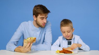 Genç bir adam ve bir çocuk masada oturuyorlar, adam çocuğun fast food yemesine izin vermiyor. Sağlıklı ve sağlıksız gıda kavramı. Fast food