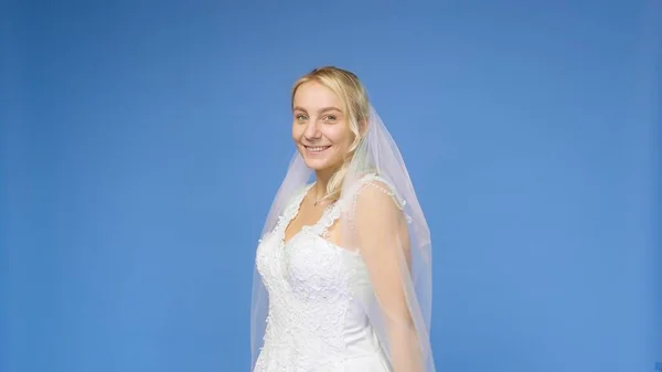 Jovem linda loira sorrindo em um vestido branco de casamento e véu em um fundo azul. A rapariga olha para a câmara. Casamento — Fotografia de Stock