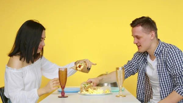Facet i dziewczyna na randce jedzą fast food i piją drinki ze szklanek na żółtym tle. Na randkę. Koncepcja zdrowej i niezdrowej żywności. Fast food — Zdjęcie stockowe