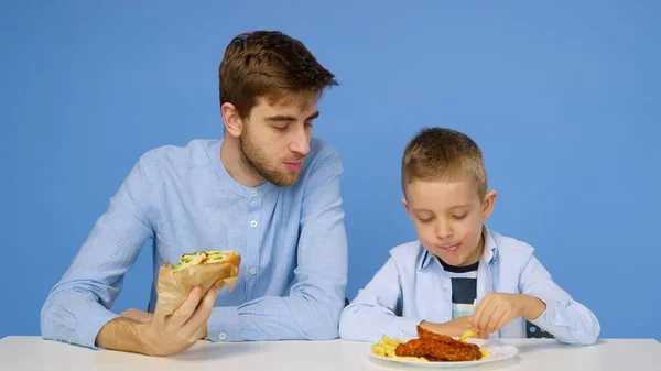 Ein junger Mann und ein Junge sitzen am Tisch, der Mann erlaubt dem Jungen nicht, Fast Food zu essen. Das Konzept der gesunden und ungesunden Ernährung. Fast food — Stockfoto