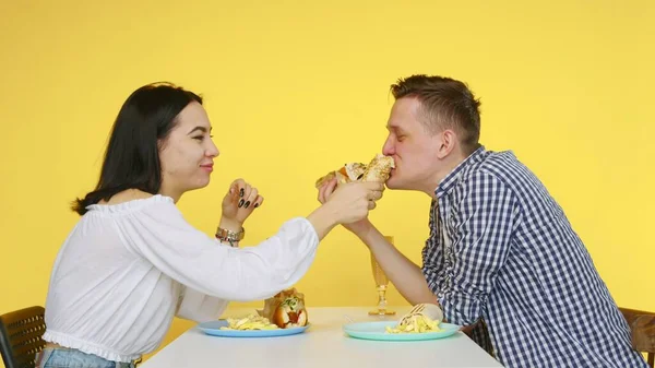 Egy pasi és egy lány egy randin gyorskaját esznek és poharakból isznak sárga alapon. Randi. Az egészséges és egészségtelen ételek fogalma. Gyorsétterem — Stock Fotó