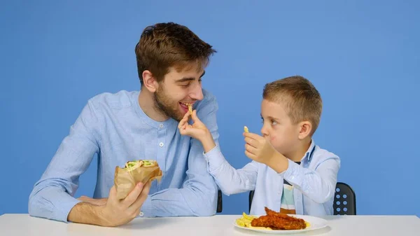 Mladý muž a chlapec sedí u stolu, muž nedovolí chlapci jíst rychlé občerstvení. Koncept zdravé a nezdravé stravy. Rychlé občerstvení — Stock fotografie