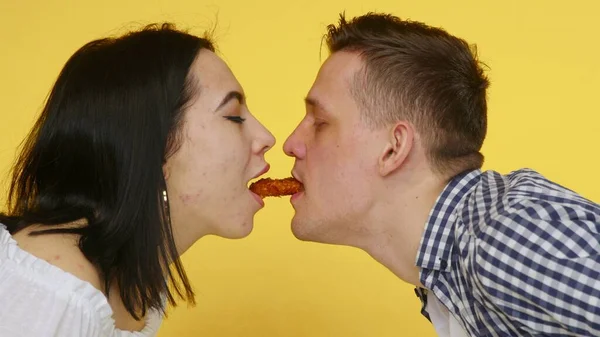 Großaufnahme einer Frau und eines Mannes, die Nuggets essen und sich zärtlich auf gelbem Grund küssen. Das Konzept der gesunden und ungesunden Ernährung. Fast food — Stockfoto