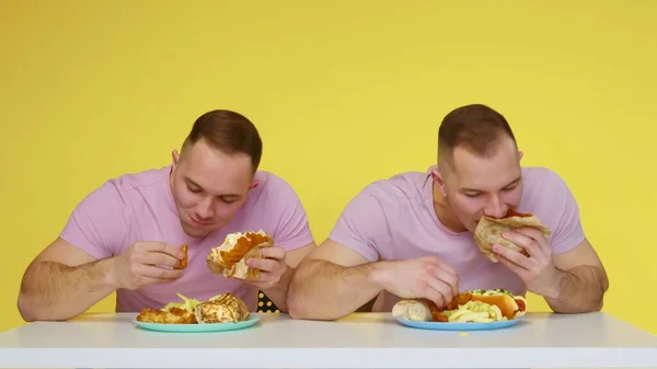 Dos gemelos fornidos comen comida rápida sobre un fondo amarillo. El concepto de comida saludable y poco saludable. Comida rápida —  Fotos de Stock