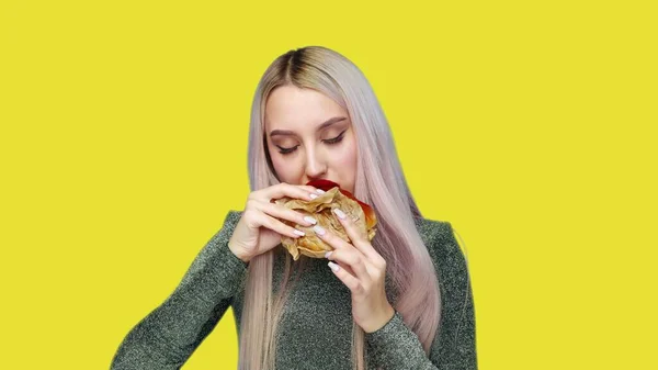 Close-up de uma menina com batom vermelho nos lábios, comendo um hambúrguer em um fundo amarelo. Dieta. O conceito de comida saudável e insalubre. fast food — Fotografia de Stock