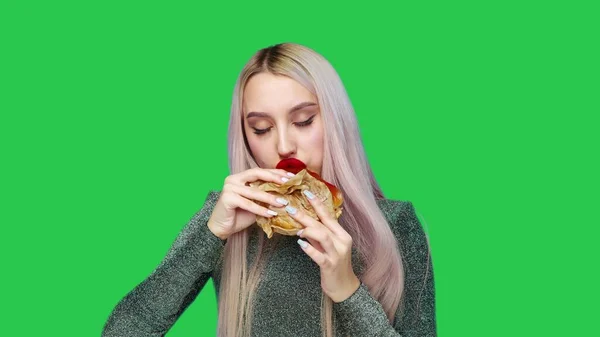 Close-up de uma menina com batom vermelho nos lábios, comendo um hambúrguer em um fundo verde. Dieta. O conceito de comida saudável e insalubre. fast food — Fotografia de Stock