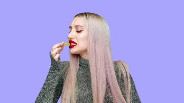 Közelkép egy lány festi az ajkait piros rúzzsal, és elkezd enni egy hamburgert örömmel a lila háttér. Fogyókúra. Az egészséges és egészségtelen ételek fogalma. gyorsétterem — Stock Fotó