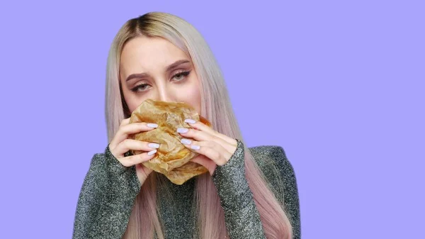 Close-up de uma menina com batom vermelho nos lábios, comendo um hambúrguer em um fundo roxo. Dieta. O conceito de comida saudável e insalubre. fast food — Fotografia de Stock