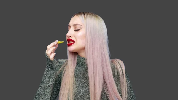 Közelkép egy lány festi az ajkait piros rúzzsal, és elkezd enni egy hamburgert örömmel szürke alapon. Fogyókúra. Az egészséges és egészségtelen ételek fogalma. gyorsétterem — Stock Fotó