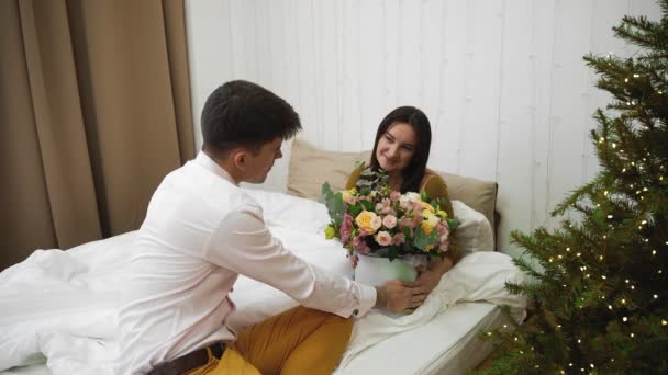 Seorang pemuda memberikan bunga untuk pacarnya, di kamar di tempat tidur. Romansa — Stok Video
