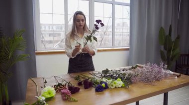 Çiçekçilikle meşgul genç ve güzel bir kadın çiçek aranjmanı için en iyi çiçekleri toplamaya başlar. Çiçek.