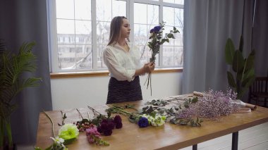 Çiçekçilikle meşgul genç ve güzel bir kadın çiçek aranjmanı için en iyi çiçekleri toplamaya başlar. Çiçek.
