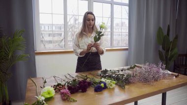 Çiçekçilikle meşgul genç ve güzel bir kadın çiçek aranjmanı için en iyi çiçekleri toplamaya başlar. Çiçek.