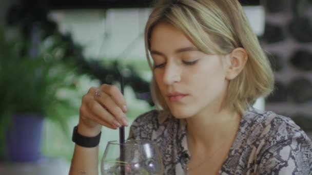Ein trauriges Mädchen sitzt in einer Bar und rührt mit einem Strohhalm einen Mojito an — Stockvideo