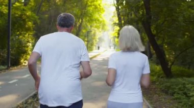 Aktif aile eğitimi. Kıdemli karı koca sabah koşularının keyfini çıkarıyorlar, halka açık parkta koşuyorlar, arkadan bakıyorlar.